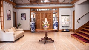 Un vestíbulo amplio con un sofá color crema, una mesa de centro de madera con un centro de mesa floral, y una escalera con alfombra roja.