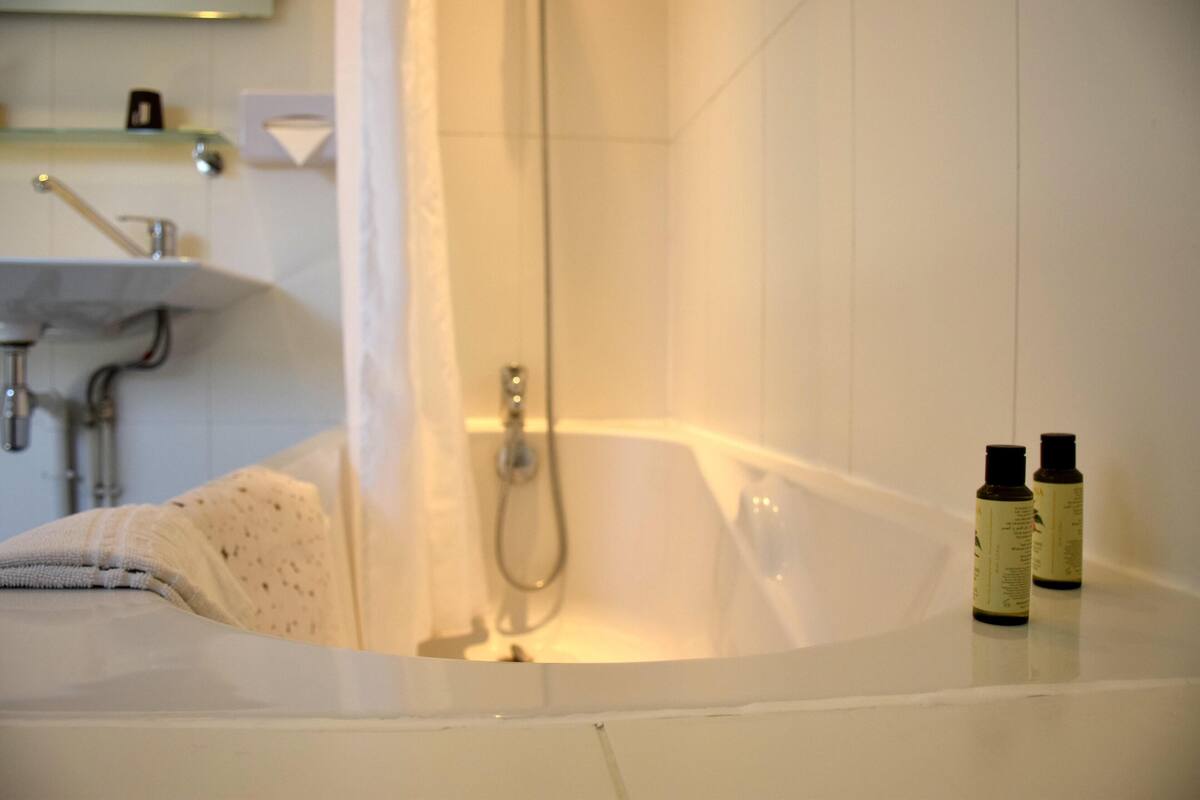 A bathtub with two bottles of lotion, a towel, and a showerhead.