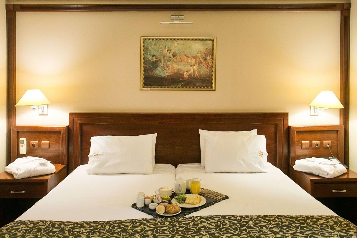 A hotel room with a large bed, two bedside tables, a painting on the wall, and a tray with breakfast items.