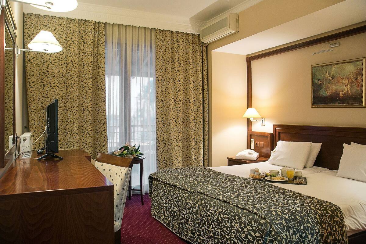 A hotel room with a bed, desk, and a painting on the wall.