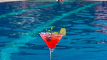 Vista clara de una piscina con un cóctel rojo en copa de martini, adornado con una hoja de menta y una rodaja de lima.