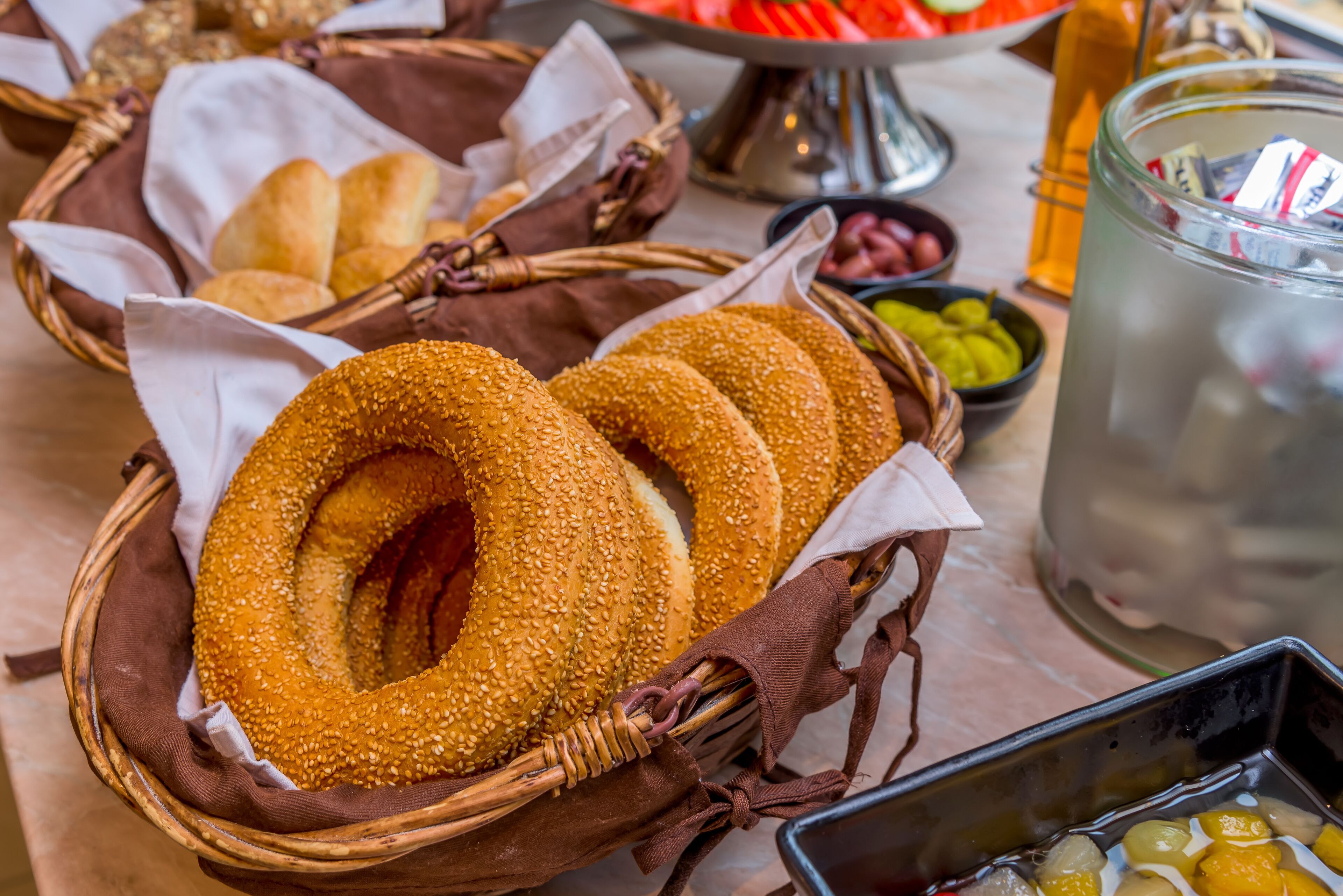 Une table avec des paniers de bagels, des bols de trempettes et une carafe d’eau.
