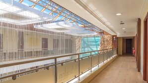 A corridor with a glass ceiling, a stone wall, and a railing. - Avalon Airport Hotel Thessaloniki (Thermi)