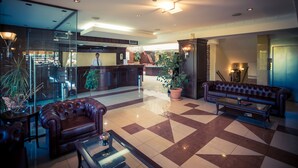 A lobby with a checkered floor, leather sofas, a reception desk, and potted plants. - Avalon Airport Hotel Thessaloniki (Thermi)