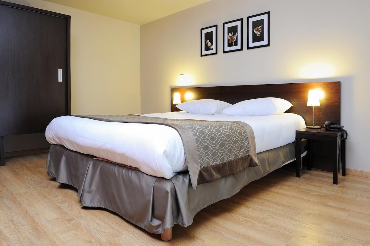 Een net opgemaakt bed met hoofdbord, een nachtkastje met lamp en een aan de muur bevestigd fotolijstje.