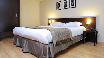 A neatly made bed with a headboard, a bedside table with a lamp, and a wall-mounted picture frame.