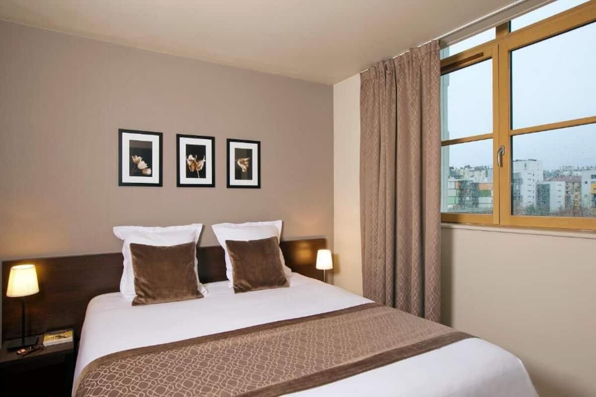 Een hotelkamer met een groot bed, twee nachtkastjes, een raam met gordijnen en drie ingelijste foto's aan de muur.