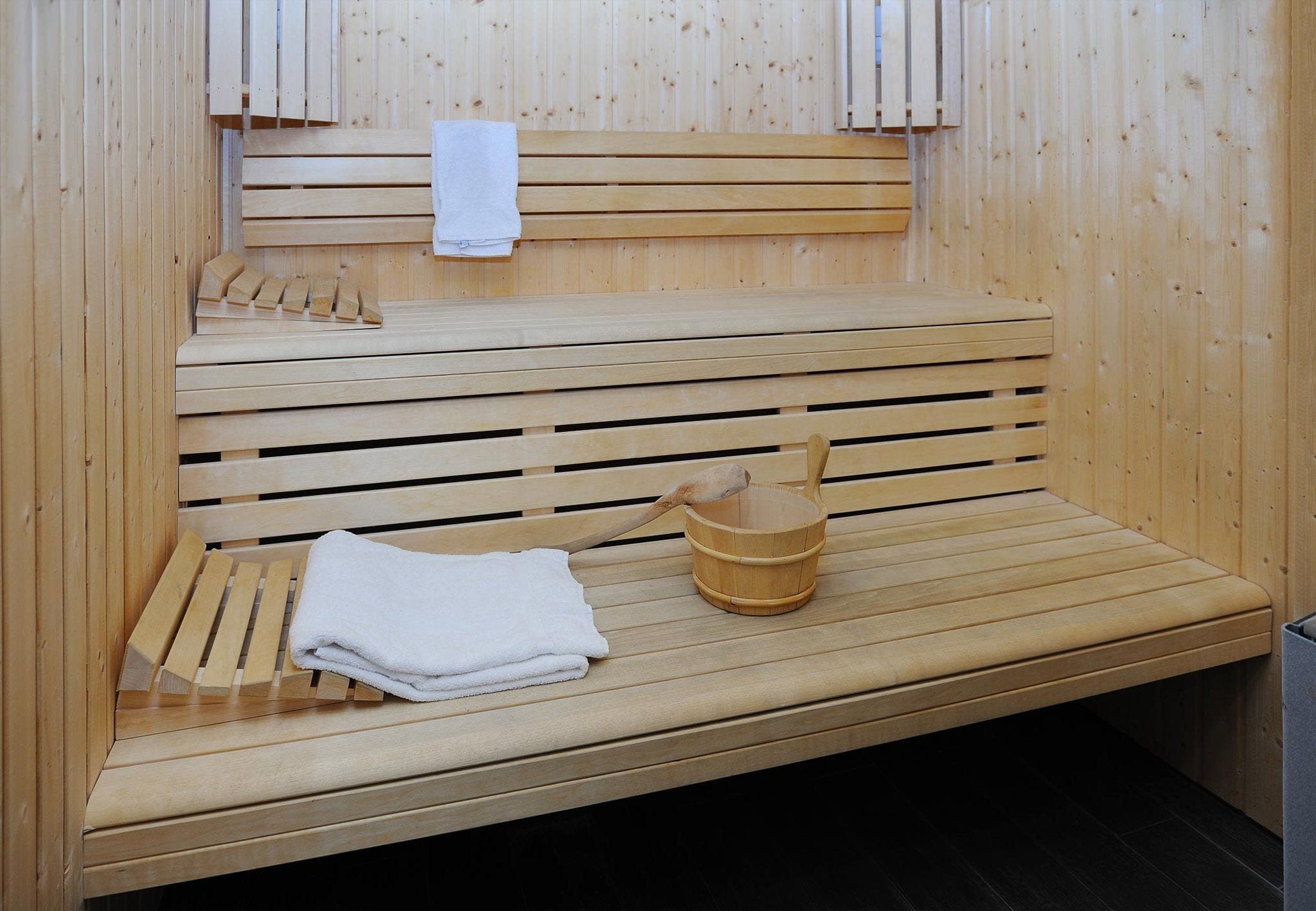 Een houten sauna bank met een houten emmer en een witte handdoek.