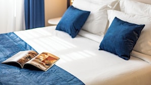 Una cama bien hecha con almohadas blancas y azules, una colcha azul y una revista encima.