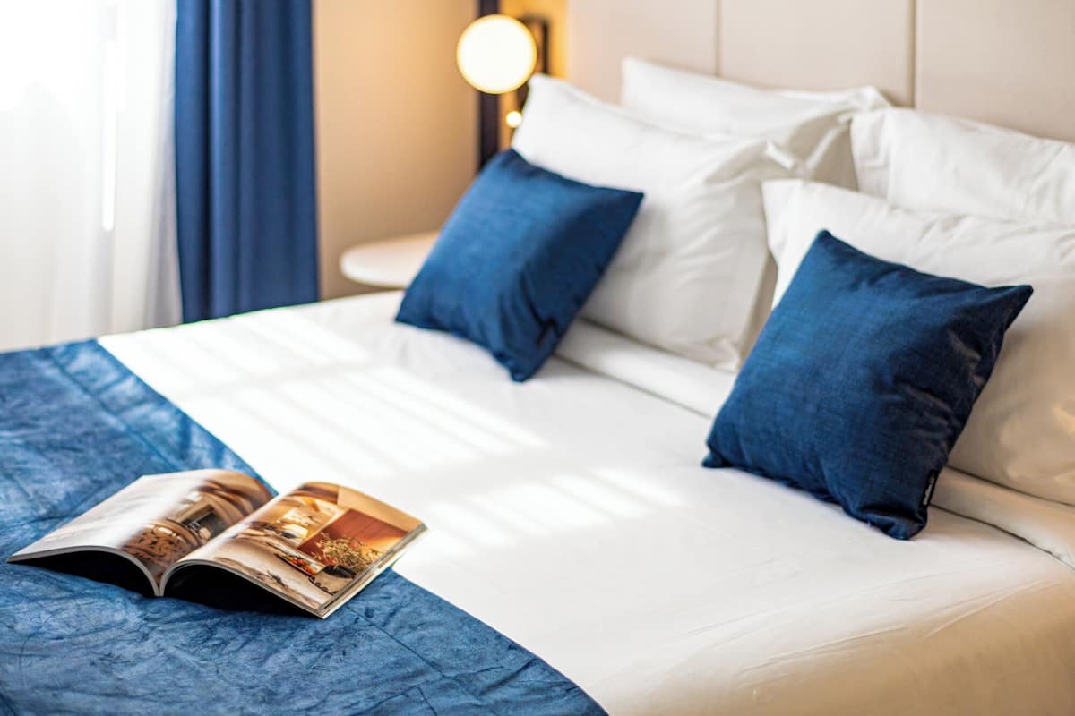 Een net opgemaakt bed met witte en blauwe kussens, een blauwe plaid en een tijdschrift op het bed.