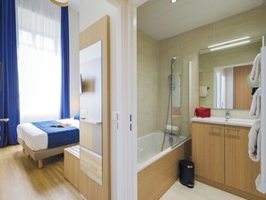 Una camera d'albergo con un letto, una doccia, un lavandino e uno specchio.