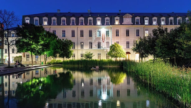 Un edificio grande e histórico con un estanque reflectante en primer plano, rodeado de árboles y un cielo nocturno despejado.