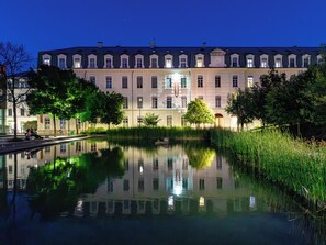 A large, historic building with a reflective pond in front, surrounded by trees and a clear night sky.