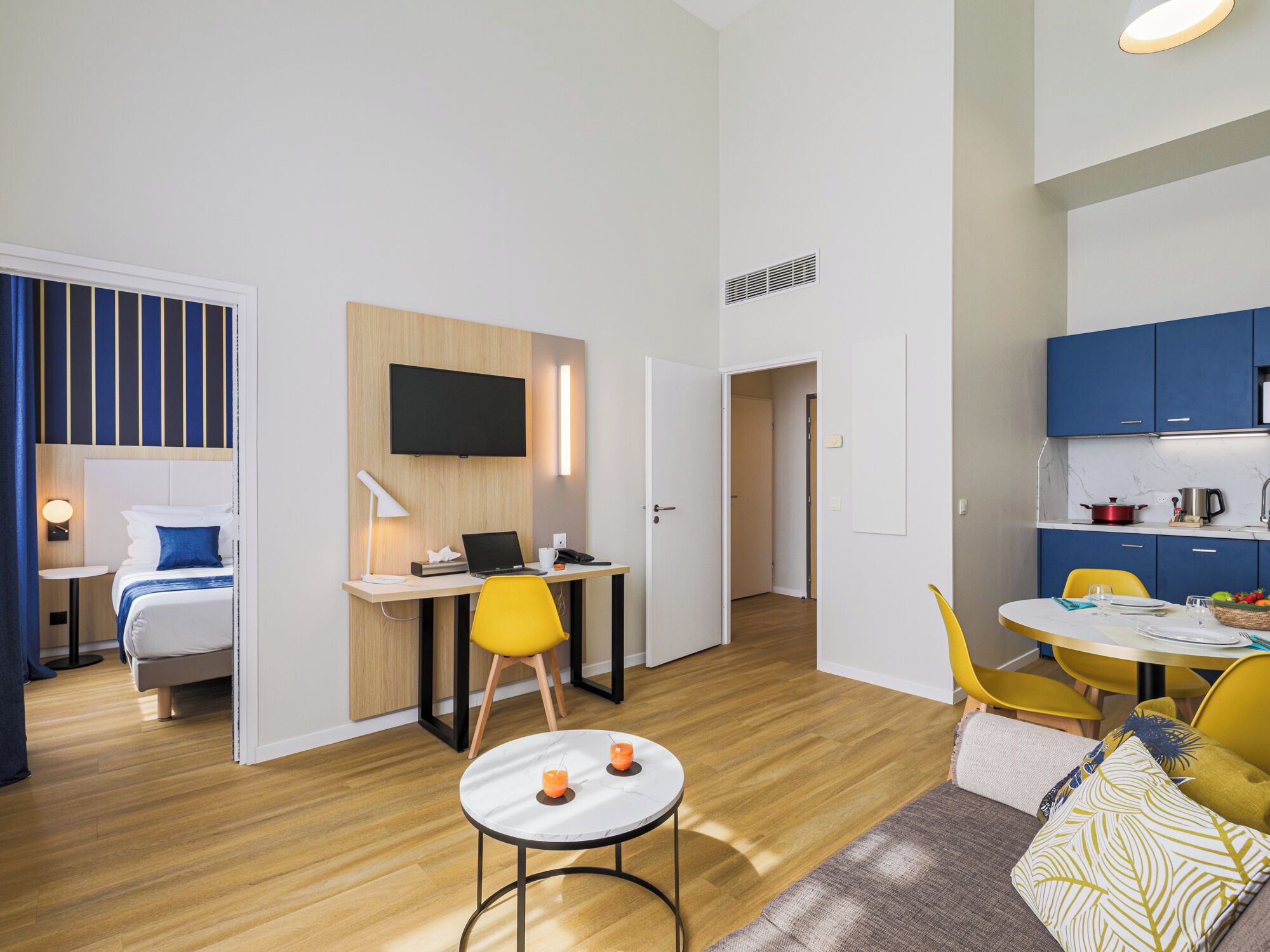 A modern hotel room with a bed, desk, laptop, and a small table with candles.