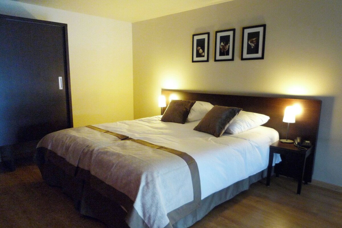 A neatly made bed with a wooden headboard, a bedside table with a lamp, and a door to the left.