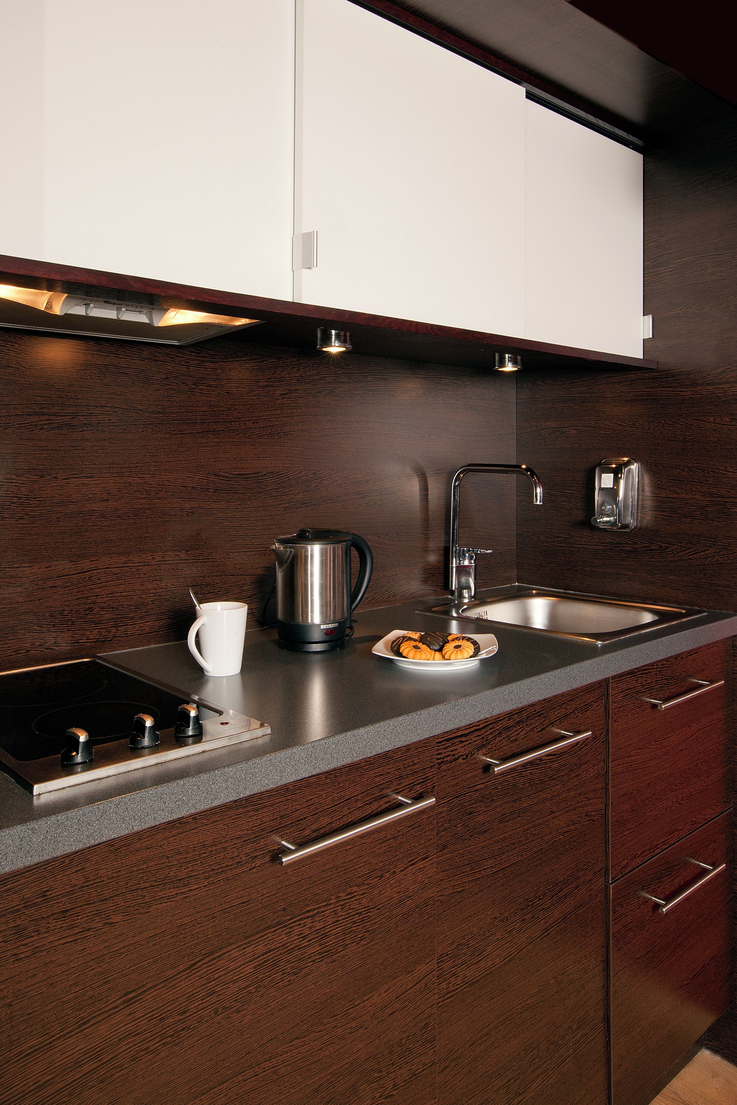 A modern kitchen with a stainless steel sink, a coffee maker, and a plate of cookies.