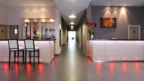 Zona de recepción de hotel con un largo pasillo, mostrador de recepción y dos taburetes de bar.