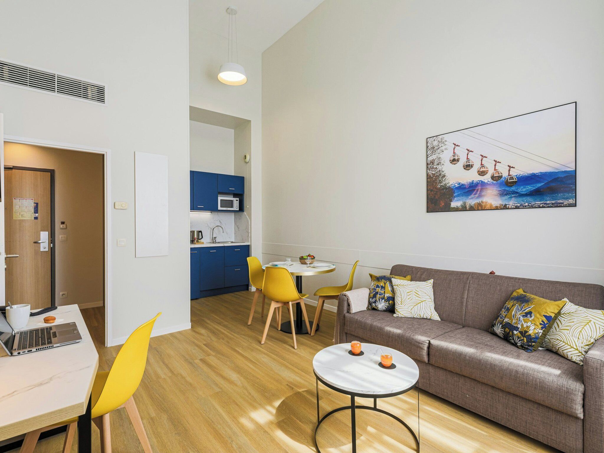 Een moderne woonkamer met een bank, een eettafel met stoelen, een keuken en een schilderij aan de muur.