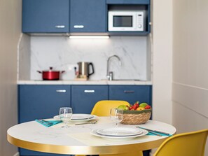 Un comedor con una mesa redonda, platos, cubiertos y una cesta de frutas.
