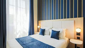 A hotel room with a large bed, two bedside tables, a headboard with vertical stripes, and a window with curtains.