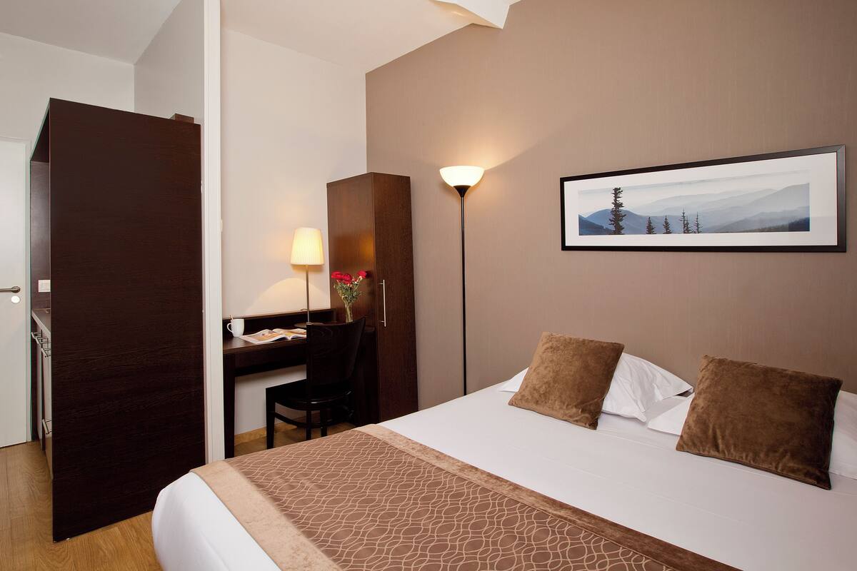 Een hotelkamer met een bed, bureau, stoel, lamp en een ingelijst schilderij aan de muur.