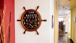 Seinälle kiinnitetty laivan ruori, jossa on teksti ”CAN BATISTE” ja erilaisia merenkulkuaiheisia symboleja.