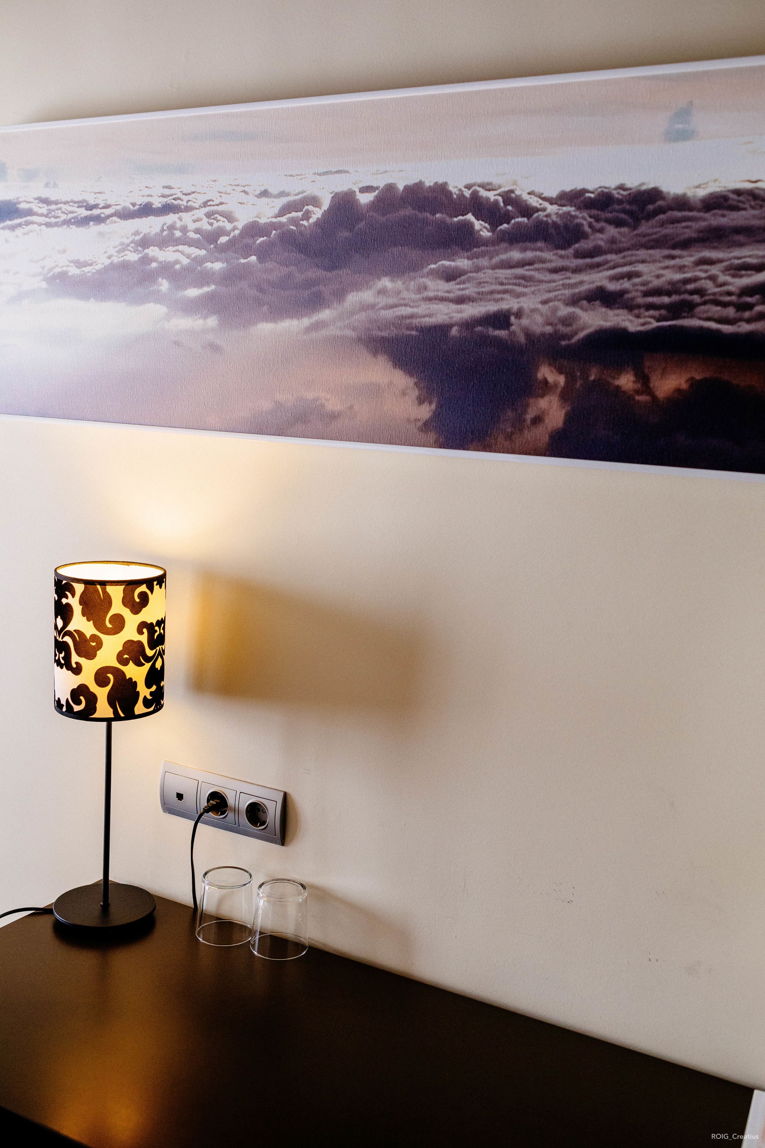 Ein Tisch mit einer Lampe und zwei Gläsern, einer Steckdose und einer Wand mit einem großen Gemälde.