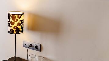 Ein Tisch mit einer Lampe und zwei Gläsern, einer Steckdose und einer Wand mit einem großen Gemälde.