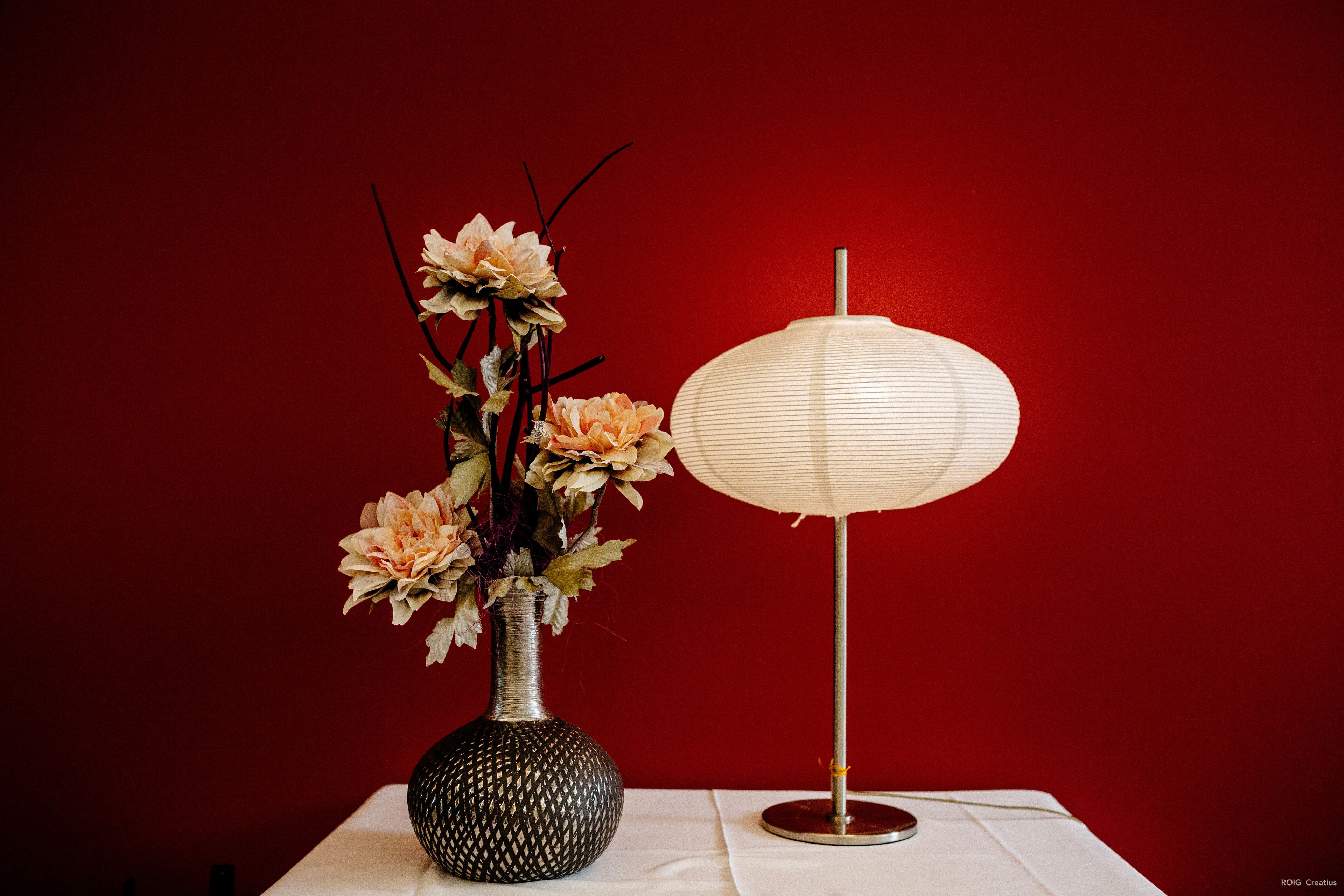 Un vase rempli de fleurs et une lampe posés sur une table, le tout sur un fond rouge.