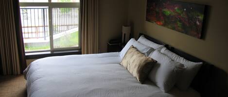 A hotel room with a large bed, a painting on the wall, and a view of a balcony with buildings.