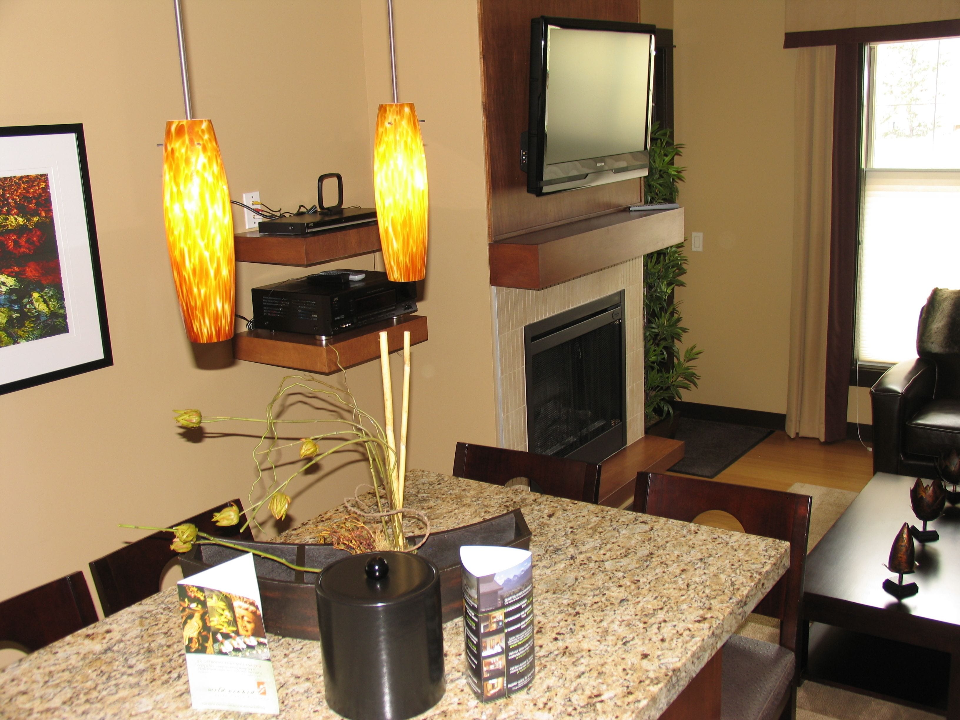 A living room with a fireplace, a television mounted above it, and a dining area with a granite countertop.