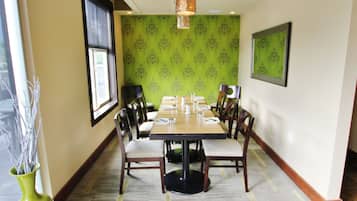 A dining area with a long table, chairs, a vase with branches, and patterned wallpaper.