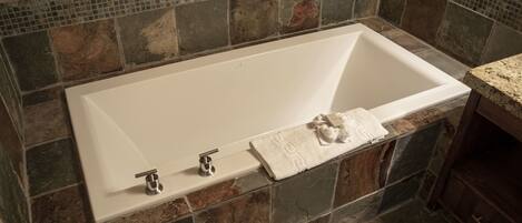 Une baignoire rectangulaire à l’intérieur blanc, placée devant un mur recouvert de mosaïques.