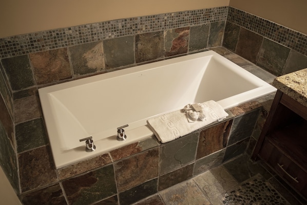 Una bañera rectangular con interior blanco, frente a una pared de mosaicos.