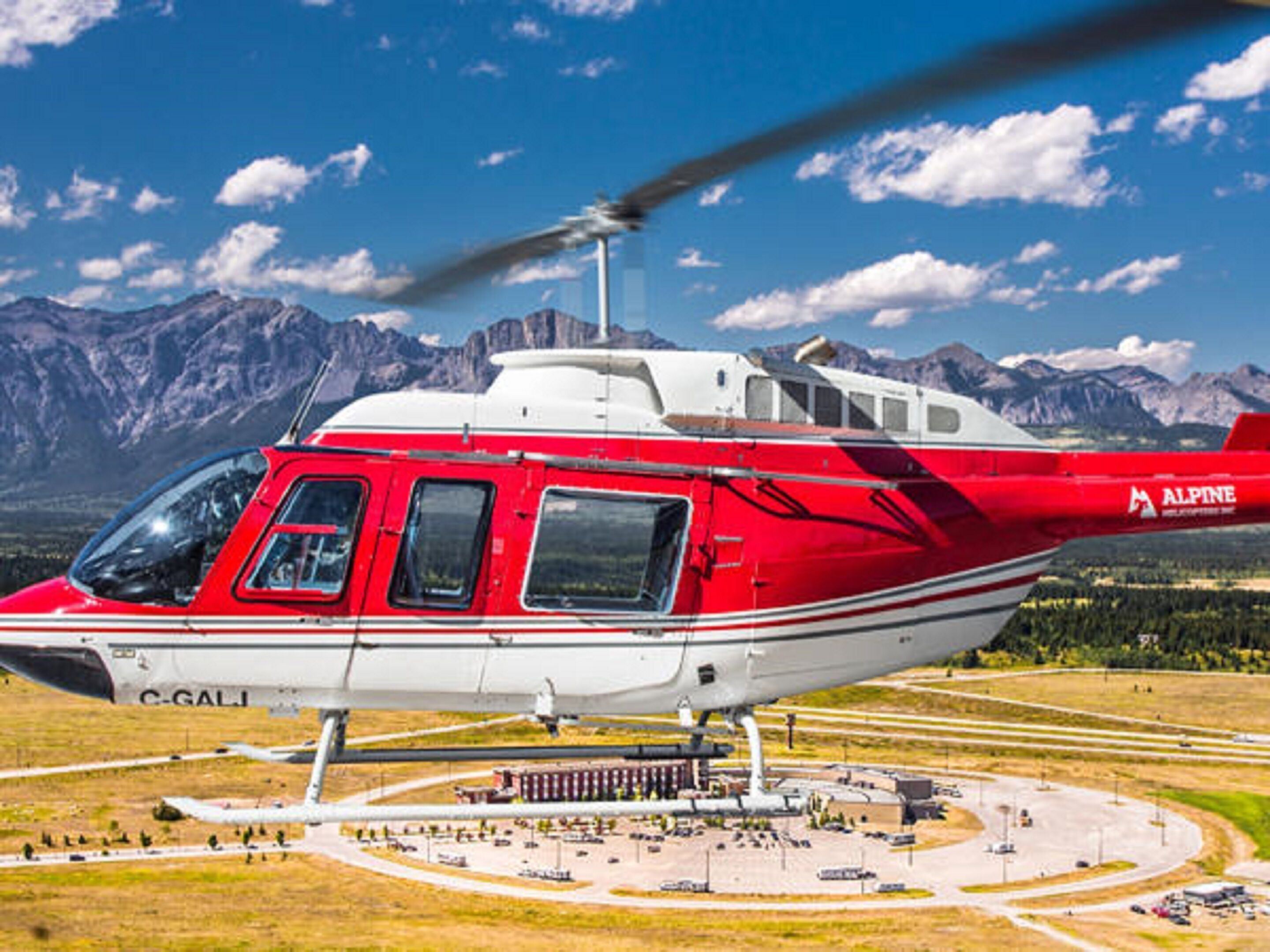 Un helicóptero rojo y blanco con el código de registro C-GALI estacionado en un helipuerto rodeado de un paisaje montañoso.