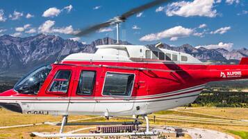 Un helicóptero rojo y blanco con el código de registro C-GALI estacionado en un helipuerto rodeado de un paisaje montañoso.