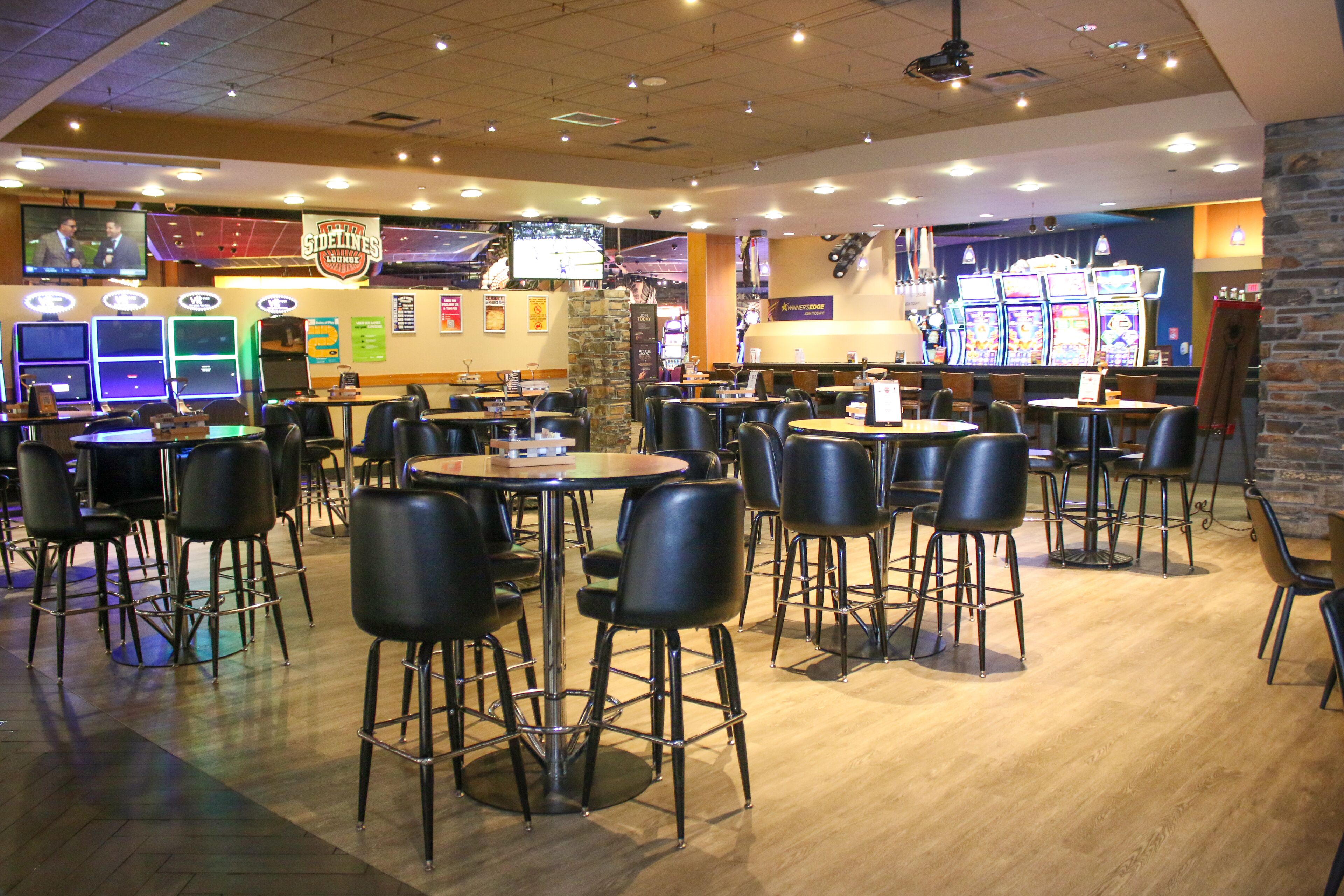 A spacious indoor area with multiple tables and chairs, a television screen, and slot machines.