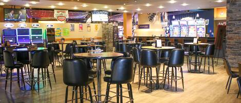 A spacious indoor area with multiple tables and chairs, a television screen, and slot machines.