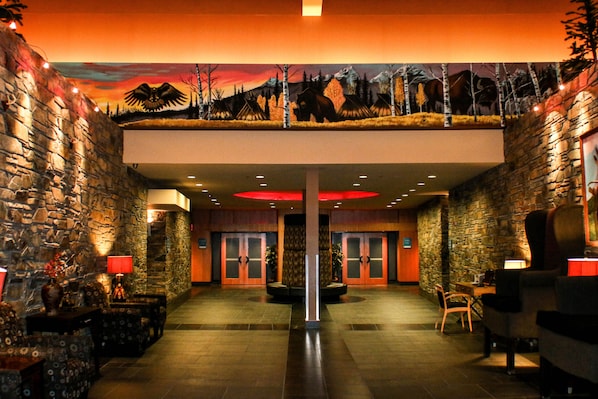 A lobby with stone walls, a central column, and a ceiling mural. There are chairs and tables with lamps.