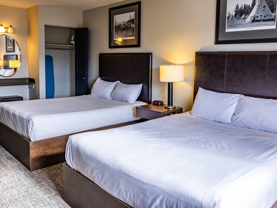 Habitación de hotel con dos camas, un escritorio, una silla, un espejo y dos cuadros en la pared.