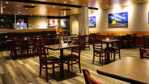 Un restaurante con suelo de madera, varias mesas y sillas, una zona de bar y obras de arte en las paredes.