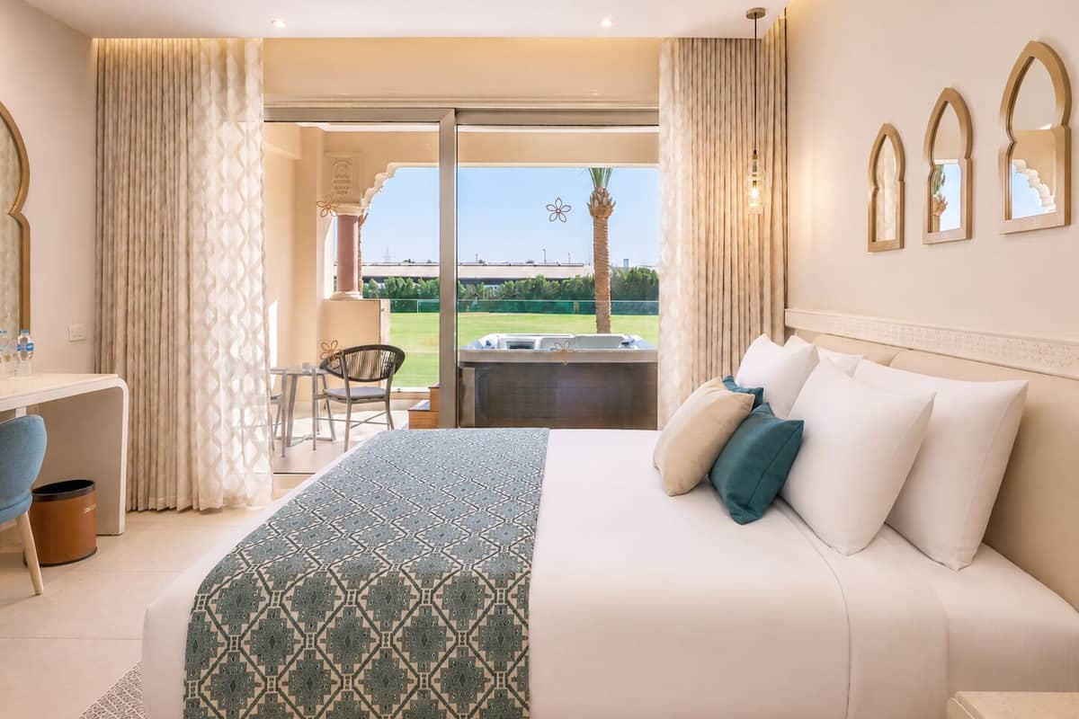 Habitación de hotel con cama, escritorio, silla y vista a una cancha de tenis.