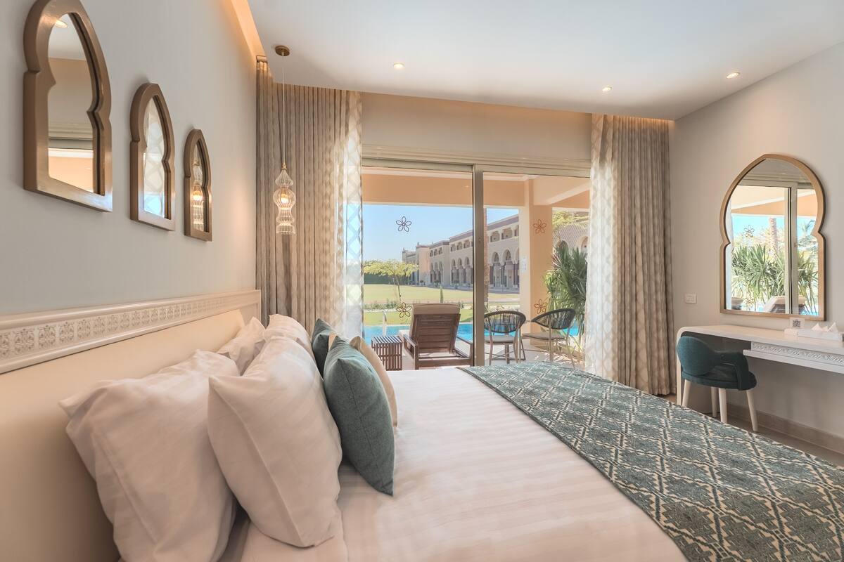 Habitación de hotel con una cama grande, un escritorio y vistas a una piscina y un edificio.