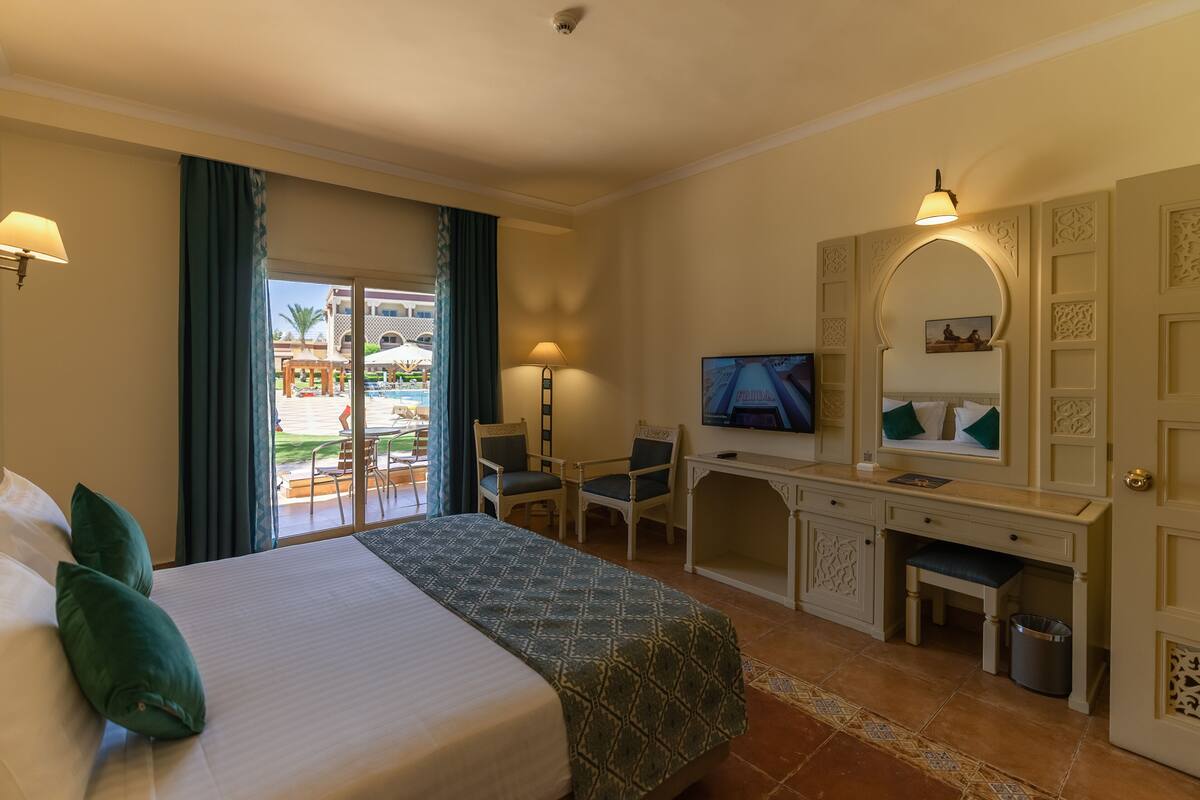 Habitación de hotel con cama, escritorio, televisión y vistas a una piscina y zona exterior.