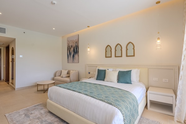 Une chambre à coucher avec un grand lit, une table de chevet, une chaise, une petite table ronde et un luminaire fixé au mur.