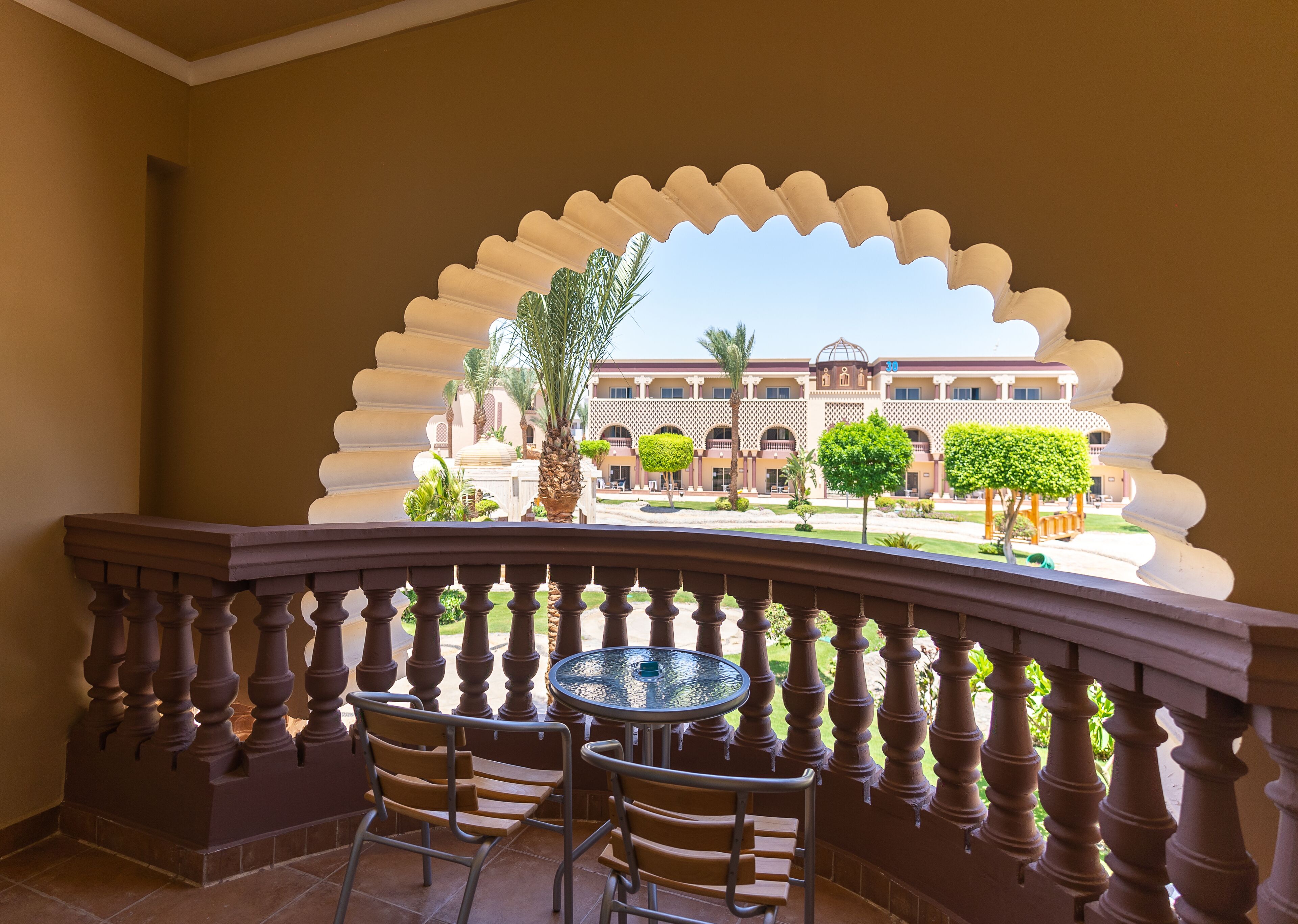 A balcony with a wrought iron railing, two wooden chairs, and a round table.