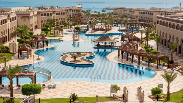 A large, multi-level swimming pool complex with multiple pools and walkways, surrounded by palm trees and architectural structures. - Sunrise Sentido Mamlouk Palace - All inclusive (Hurghada)