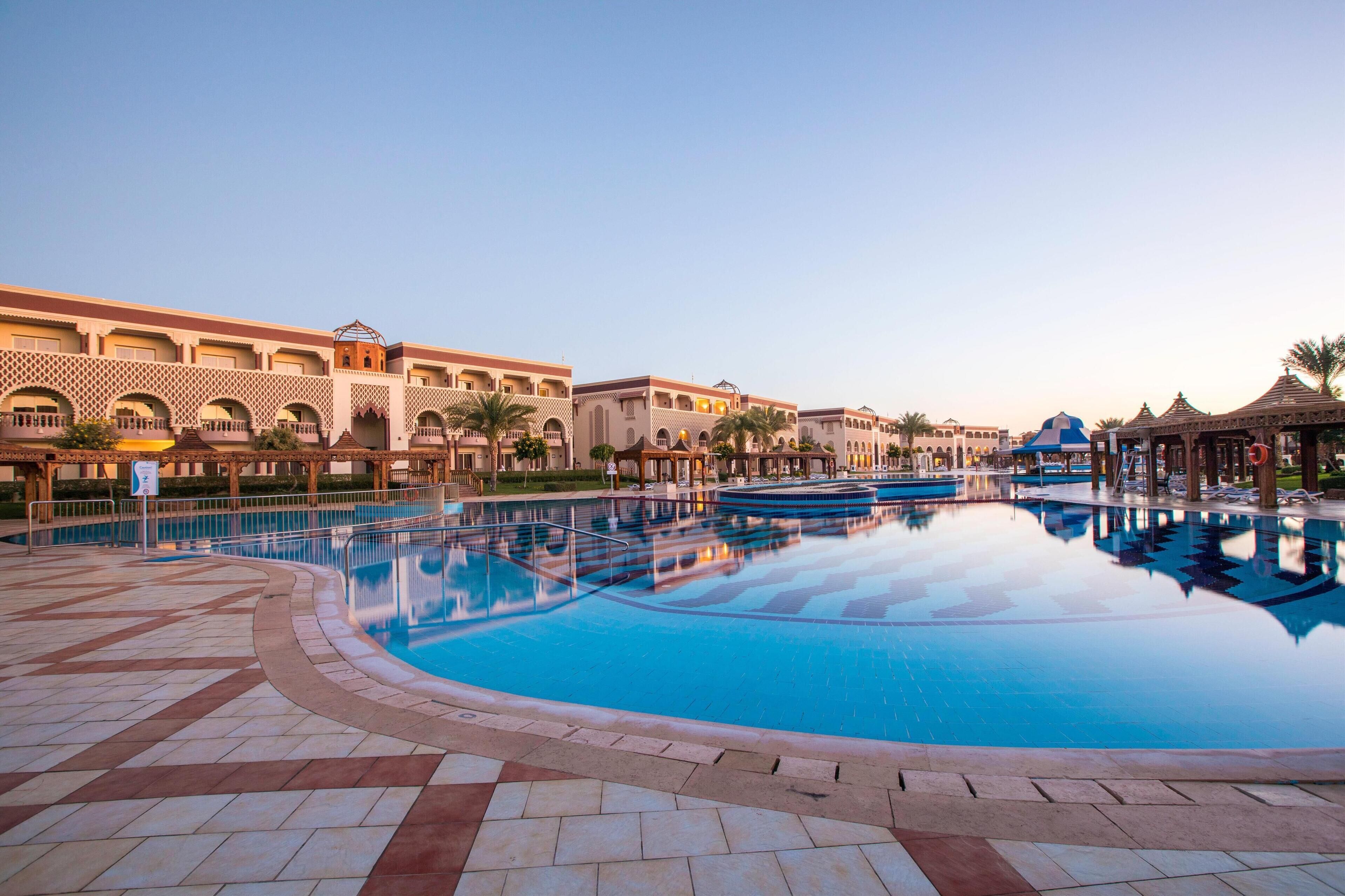 A swimming pool with a reflection of a building with arched windows and a tiled walkway.