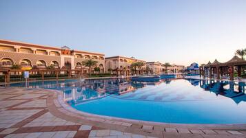 A swimming pool with a reflection of a building with arched windows and a tiled walkway.