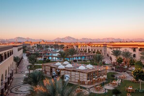A hotel courtyard with a pool, palm trees, and a view of mountains. - Sunrise Sentido Mamlouk Palace - All inclusive (Hurghada)